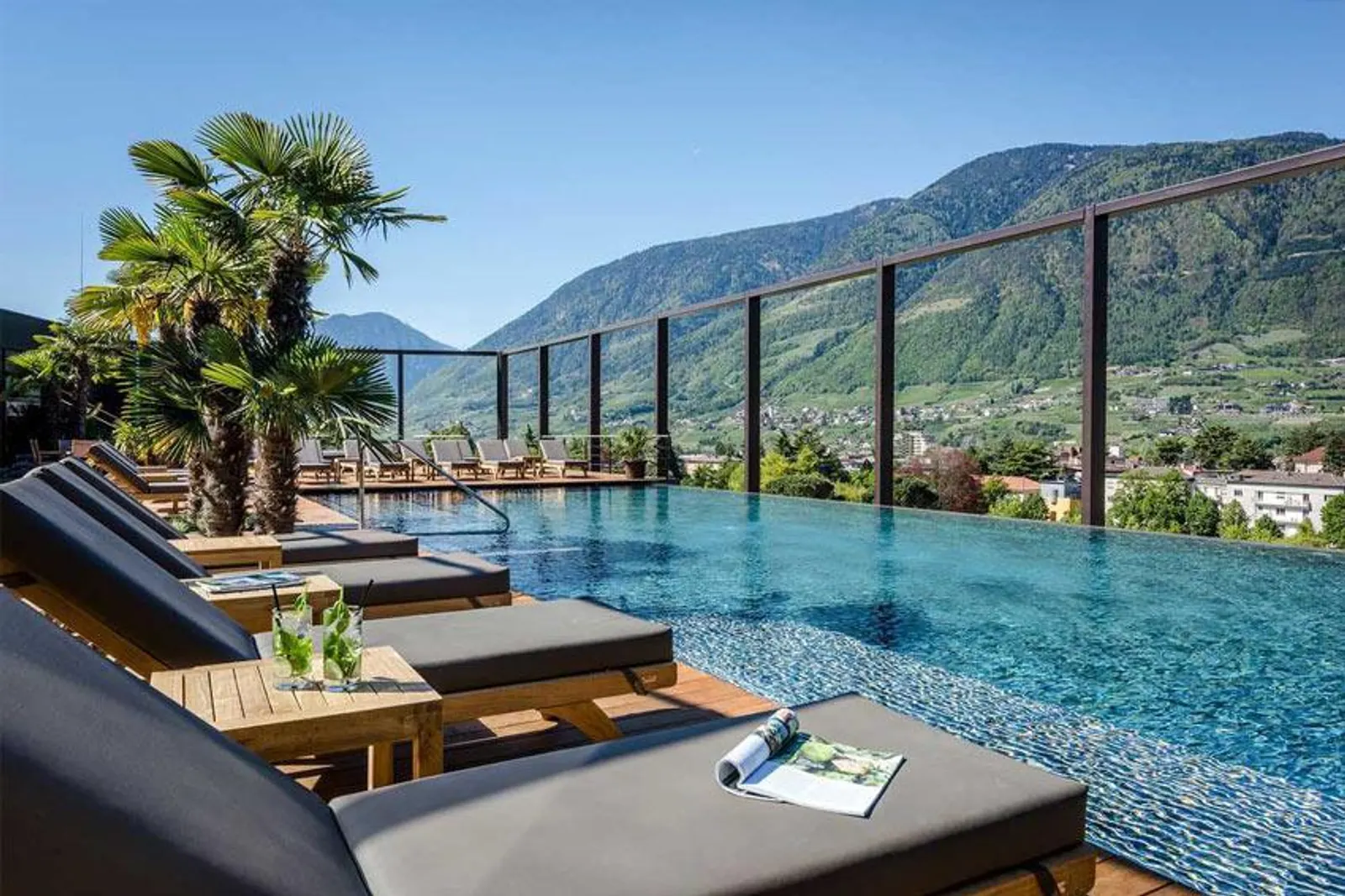 Piscina a sfioro sul tetto di un hotel di montagna, lettini e vista sulle Alpi.