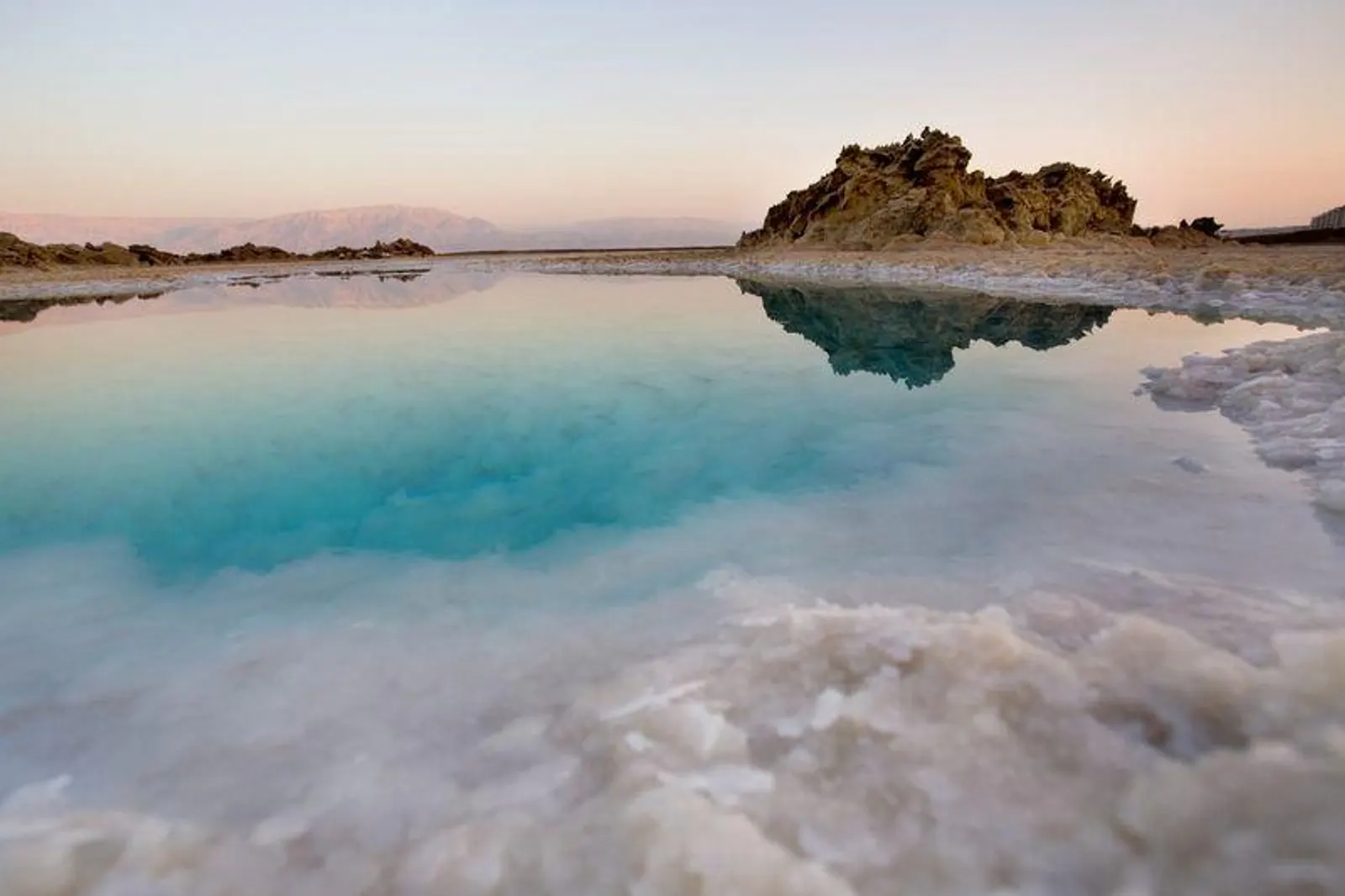 Piscina salina naturale al tramonto, rocce bianche di sale e acqua turchese.